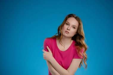 Stüdyoda pembe gömlekle poz veren bir kadın var. İfadesi, özgüven ve içgözlem karışımı bir şey ifade ediyor, koyu mavi bir arkaplan üzerine kurulu..