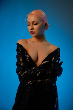 Bir kadın zarif bir şekilde poz verir. Yumuşak bir ışık ve açık mavi bir arkaplan, giyimi ve ifadesiyle zarafetini gösterir..