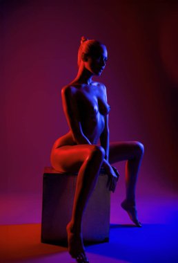 Bir model, stüdyodaki kırmızı ve mavi ışıklarla aydınlatılmış bir kutunun üzerinde zarifçe oturur..