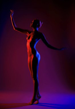 Bir dansçı zarifçe poz verir, parlak kırmızı ve mavi ışıklarla aydınlanır..
