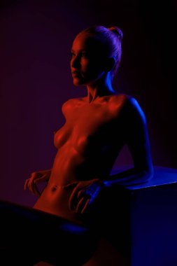 Çarpıcı kırmızı ve mavi ışıkta duran bir model, koyu bir ortamda kendine güvenen bir ifade ve zarif bir duruş sergiliyor..