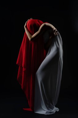 Bir kadın, bir döküm oturumunda dramatik bir şekilde poz verir, kırmızı ve beyaz kumaşların bir karışımını koyu arka planda gösterir..