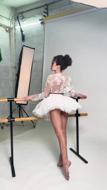 Kadın zarif bir şekilde stüdyo ortamında soyunmadan poz veriyor, sahne arkasında zarafet ve sanatçılık sergiliyor..