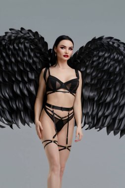 Kendine güvenen bir kadın, etkileyici kanatları, somut güzelliği ve gücü olan şık siyah iç çamaşırlarını sergiler..