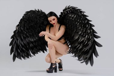 Bir kadın, büyük siyah kanatlarla süslenmiş iç çamaşırlarıyla bir stüdyo ortamında güzelliğini sergiliyor..