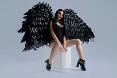 Güzel bir kadın zarif bir şekilde oturur, siyah iç çamaşırını ve etkileyici kanatlarını göstererek büyüleyici bir cazibe yaratır..