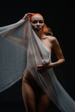 Saf kumaşlı, kendine güvenen kızıl saçlı bir kadın esmer bir arkaplana karşı poz verir..