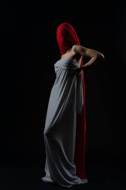 Model, karanlık bir stüdyoda akıcı kumaşla eşsiz bir stil sergiliyor, zarafet ve sanatsal ifade vurgulanıyor..