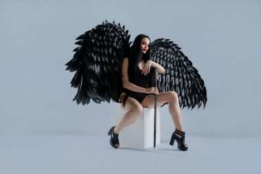 Bir kadın, stüdyo ortamında karmaşık iç çamaşırları ve dramatik siyah kanatlar giyerken kendine güveni resmediyor..