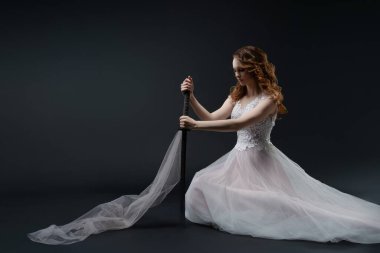 Narin iç çamaşırları giyen bir gelin zarif bir şekilde yerde oturur, kumaşı tutar ve bir stüdyoda güzelliğini gösterir..