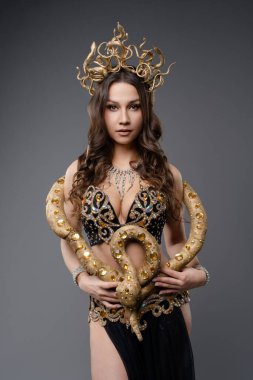 Özenle hazırlanmış altın ve siyah kıyafetlerle süslenmiş bir model, bir yılanı tutuyor, büyüleyici bir güzellik ve sanatsal karışım sergiliyor..
