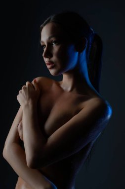Yumuşak bir ışık ortamında üstsüz poz veren bir kadın samimiyet ve hassasiyeti ifade eder, sakin bir atmosfer yaratır..