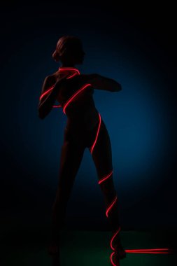 Güzel bir kadın zarif bir şekilde ayakta duruyor. Stüdyoda parıldayan kırmızı ışıkla betimlenmiş şekli. Atmosfer sanatsal ve büyüleyici..