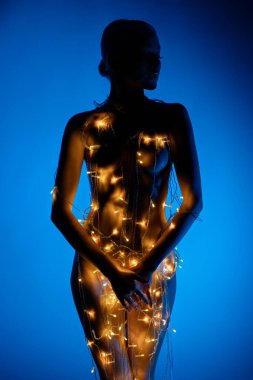 Bir kadın zarif bir şekilde durur, parlak ışıklarla süslenir, büyüleyici bir siluet yaratır, mavi bir arka plana karşı..