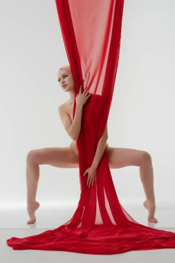 Bir kadın, dalgalı kırmızı kumaşı tutarken güzellik yayar, basit, aydınlık bir alanda çarpıcı bir görüntü yaratır, bu da vücudunu ön plana çıkarır..
