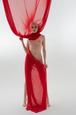 Çıplak bir kadın zarif bir şekilde kırmızı kumaşla örtülmüş, parlak, minimalist stüdyo alanında güzellik ve kendine güven sergiliyor..