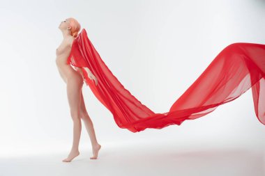 Bir kadın zarif, üstsüz ve çıplak, kırmızı bir kumaşa bürünmüş, iyi aydınlatılmış bir stüdyoya güzellik ve güven saçar..