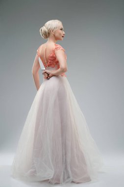 Bir stüdyo ortamında, bir kadın zarif bir gelinlik içinde, çarpıcı detaylar içeriyor. Sırtı dönük, ve kan lekeleri hassas kumaşa karşı keskin bir kontrastla, güzellik ve dehşetin ürkütücü bir karışımını oluşturuyor..