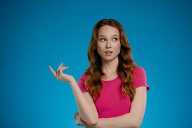 Stüdyoda parlak mavi bir arka planı olan bir kadın neşeli bir ifade sergiliyor. Kendine güveni ve jesti bir kişilik ve duygu duygusu yansıtıyor, dikkat çekiyor..