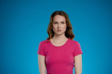 Stüdyoda kendine güvenen bir kadın ifadesiyle çeşitli duygular sunuyor. Onun parlak pembe gömleği parlak mavi arka planla güzel tezat oluşturuyor..