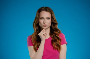 Parlak bir stüdyoda, bir kadın neşeli bir ifadeyle ayakta duruyor, düşünürken parmağını dudağında dinlendiriyor. Onun uzun, dalgalı saçları ve pembe gömleği hayat dolu atmosfere ekleniyor..