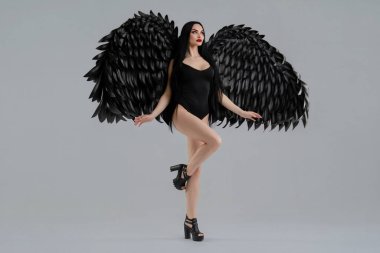 Bir kadın, büyük siyah kanatlarla tamamlanmış iç çamaşırlarıyla güzellik sergiliyor. Kendine güven ve zarafet saçıyor..