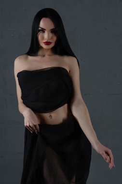 Kendine güvenen bir kadın zarif siyah iç çamaşırlarıyla güzelliğini sergiliyor, kısmen akıcı kumaşla örtülmüş, poz veriyor..