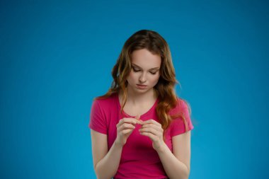 Pembe bluzlu bir kadın stüdyoda poz verirken ellerine odaklanır. Mavi arka plan onun düşünceli duygularını arttırıyor ve düşünceli davranışlarını vurguluyor..