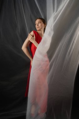 Bir stüdyo ortamında, dalgalı kırmızı elbiseler giymiş bir kadın duruşuyla, etkileyici bakışları ve zarif vücut diliyle bir dizi duygu aktarıyor..