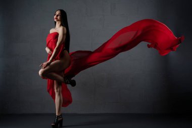 Kendine güvenen bir kadın zarif bir şekilde kırmızı iç çamaşırıyla poz verir ve zarif bir kumaşla güzelliğini sergiler..