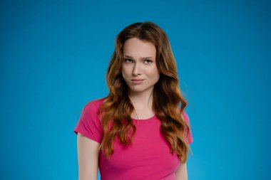 Bir kadın stüdyo ortamında poz veriyor, saçlarında dalgalarla neşeli bir ifade sergiliyor. Parlak mavi arka plan onun neşeli tavırlarını arttırıyor, davetkar bir atmosfer yaratıyor..