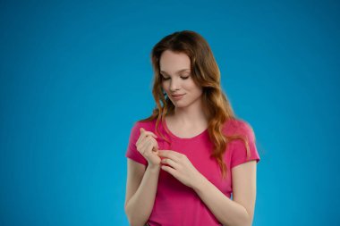 Pembe bluz giymiş bir kadın stüdyoda duruyor. Düşünceli bir duruş sergiliyor, bir dizi duygu sergiliyor. Saçları, parlak mavi bir arkaplanda yüzünü yumuşakça çerçeveliyor..