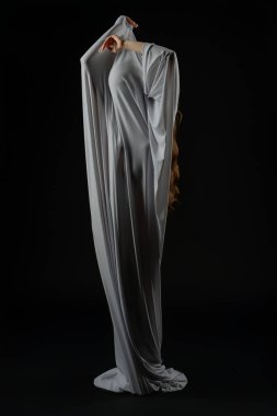 Bir kadın zarif bir kıyafetle poz verir, formunu ve zarafetini yumuşak ışık altında gösterir..