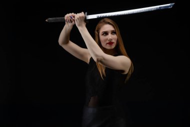 Güzel bir kadın kendinden emin bir şekilde bir kılıç tutuyor, loş bir alanda zarif iç çamaşırları giyerken sert bir poz veriyor..