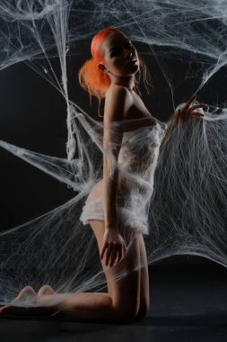 Güzel kızıl saçlı bir kadın şeffaf bir ağ tuzağının içinde zarifçe poz verir, zarafetini ve gücünü ön plana çıkarır..