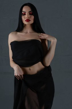 Kendine güvenen bir kadın zarif bir şekilde poz verir, siyah iç çamaşırlarını göstererek zarif bir kumaşla sarmalanır, saf bir güzellikle.