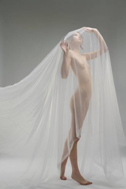 Bir kadın kendinden emin, katıksız kumaşa bürünmüş, minimalist kapalı bir ortamda güzelliğini ve zarafetini sergiliyor..