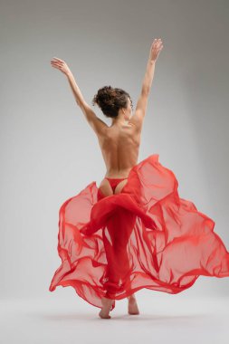 Bir kadın zarif bir şekilde dans eder, atletizm ve sanatını sergilerken kırmızı bir kumaşa sarınır. Işık ve gölgeler anı güçlendirir.