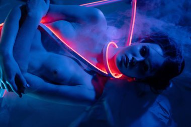 Bir kadın zarif bir şekilde neon ışıkların ve sislerin oluşturduğu yaratıcı bir düzende, sanatsal bir şekilde güzellik ve kendine güven sergiliyor..