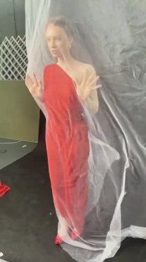 Bir model, stüdyo ortamında saf kumaşla etkileşime girerken çarpıcı kırmızı elbisesini gösteriyor..