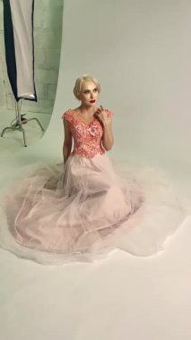 Zarif bir model güzel bir elbisenin içinde diz çöker ve iyi ışıklandırılmış bir stüdyoda bir sonraki çekim için hazırlanır..