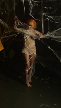 Kırmızı giyinmiş çarpıcı bir kadın zarif ipek ipliklerden oluşan geniş bir ağ içinde dans ediyor, güzelliğini ve zarafetini sergiliyor..