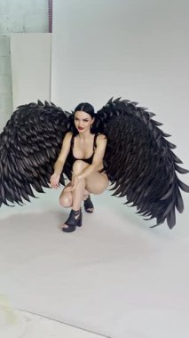 Bir kadın stüdyoda zarif bir şekilde poz verir. Güzelliğini ve özgüvenini kucaklarken siyah tüylü kanatlar sergiler..