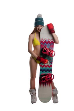 Bikini ve kış aksesuarları giyen genç bir kadın kar altında maceraya hazır bir snowboard tutuyor..