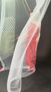 Saf kumaşla kaplanmış bir model stüdyoda poz veriyor ve ruhani bir atmosfer yaratıyor..