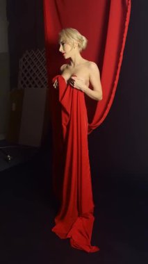 Zarif bir model güzel ışıklandırılmış bir stüdyoda akıcı kırmızı kumaş ile zarif bir poz veriyor, sanatsal ve stil sergiliyor..