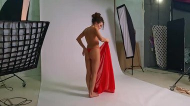 Uçsuz bucaksız bir dans stüdyosunda, güzel bir kadın duruş sergiliyor, zarafetini sergiliyor ve kırmızı bir kumaşa dokunuyor. Bu sanatsal an, hareket ve zarafet odaklı dans ve ifade ruhunu yakalar..