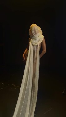 Kırmızı bir kadın, minimalist bir stüdyo ortamında zarif bir kumaş sergiliyor. Hareketlerle güzellik ve sanatın altını çiziyor..