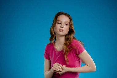 Stüdyoda, bir kadın çarpıcı bir mavi arkaplan karşısında güçlü duygular sergiler. Kendine güveni ve duruşu sanatsal açıdan güçlü bir varlık gösteriyor..