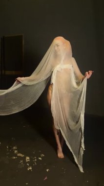 Kırmızı giyinmiş kendine güvenen bir kadın stüdyoda zarif bir şekilde dolaşıyor ve etrafındaki kumaşla olan bağlantısını gösteriyor..